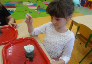 Dziewczynka trzyma w ręku pipetę, przygląda się jak zielona ciecz przenika przez piankę.